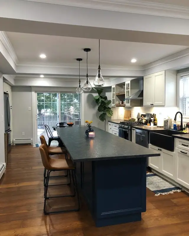 Kitchen with a long navy island, dark stone countertop, white cabinets and three glass pendant lights