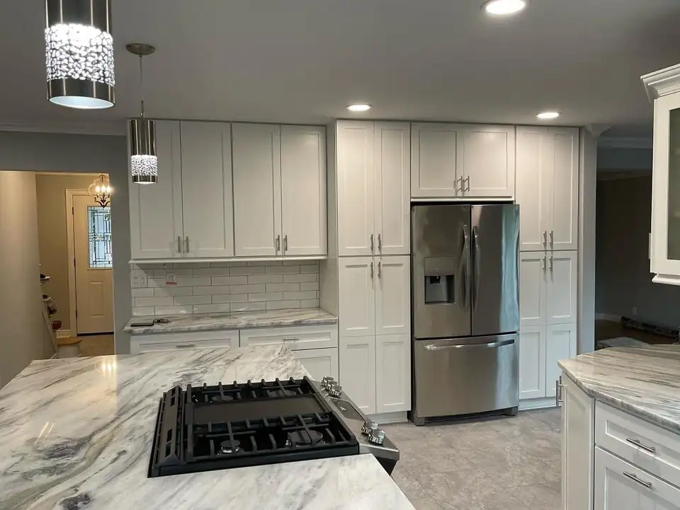 White shaker kitchen with a swirled stone island cooktop and tall pantry cabinets by The Expert Touch, home remodeling in Toms River, NJ