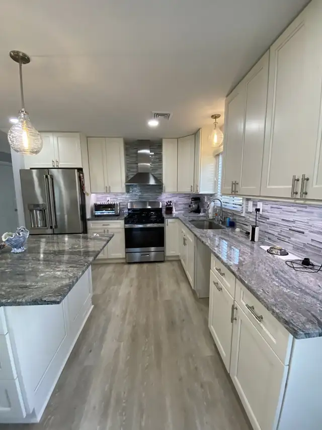 White kitchen with gray and white granite countertops, stainless appliances and mosaic backsplash