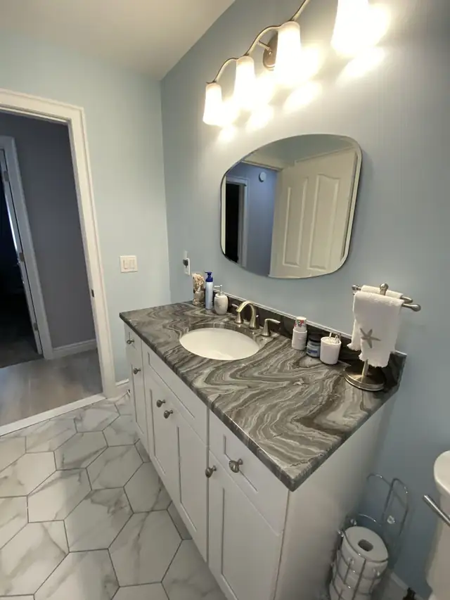 Bathroom vanity with a swirled gray stone top, an oval sink and a rounded mirror